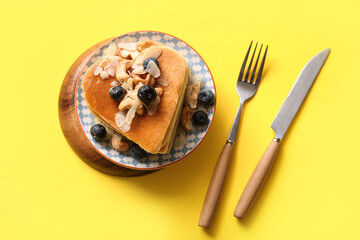Plate with tasty pancakes in shape of heart, blueberry and nuts on yellow background. Valentine's Day celebration