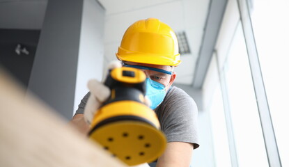 Close-up of construction worker using sander machine wearing protective yellow helmet and gloves....