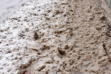 Footprints in dirty snow, slush mixed with mud, difficulty to move around the city on the dirty messy unplowed sidewalk after snowfall. Dirty snow on the road, hazardous for walking, selective focus