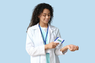 Female African-American medical intern with infrared thermometer on blue background