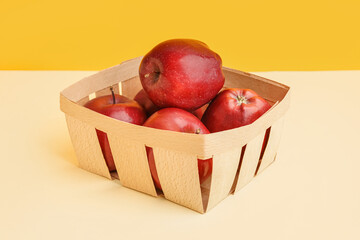 Basket with fresh red apples on colorful background
