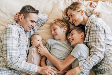 Parents and three children lie on the bed and bonding. Family happiness, time together between mom...