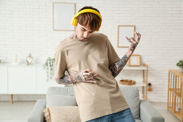Young tattooed man with headphones dancing at home