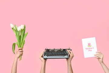 Hands holding vintage typewriter, tulips and festive postcard with text HAPPY WOMEN'S DAY on pink...