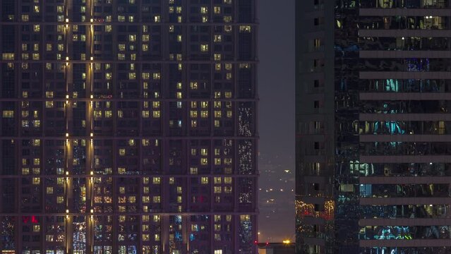 Tall blocks of flats with many glowing windows located in residential district of city aerial timelapse. Evening light in rooms in big towers and skyscrapers