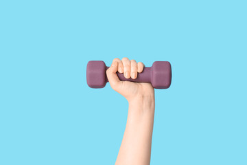 Female hand with purple dumbbell on color background, closeup