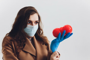 Scared young woman in medical mask standing over gray background with blurry red virus molecules.
