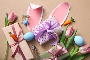 Easter eggs with gift boxes, flowers and paper bunny ears on beige background