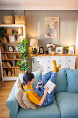 Woman reading a book and drinking coffee while relaxing at home