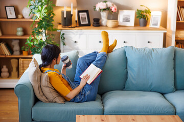 Woman drinking coffee and reading a book while relaxing at home