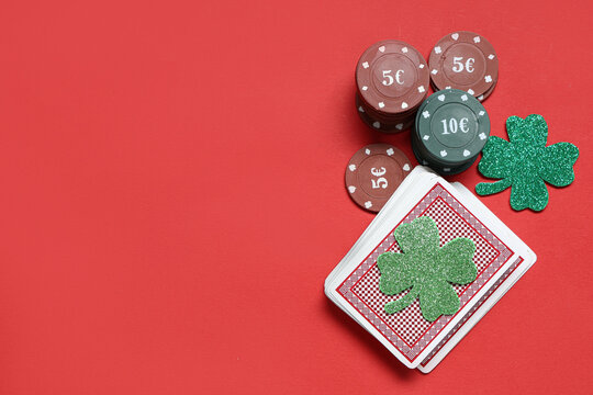 Poker chips, deck of cards and lucky clovers on red background. St. Patrick's Day celebration
