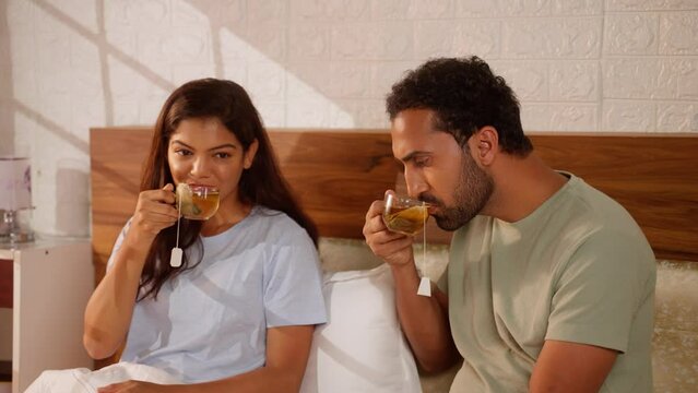 Joyful Indian couples enjoying morning Green tea on bed after wake up at bedroom - concept of antioxidants, relationship bonding, herbal beverage