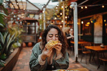 Portrait of young woman eating a delicious taco in restaurant outdoors