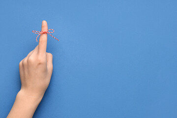 Female hand with red bow on index finger against blue background. Reminder concept
