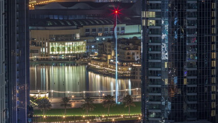Aerial view of Dubai Fountain in downtown with palms in park next to shopping mall and souq all night timelapse, UAE