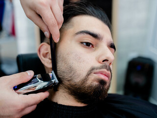A man sitting in a barbers chair having his beard trimmed