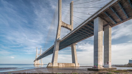 Obraz premium Vasco da Gama bridge timelapse hyperlapse with water in river and blue cloudy sky. Lisbon, Portugal.