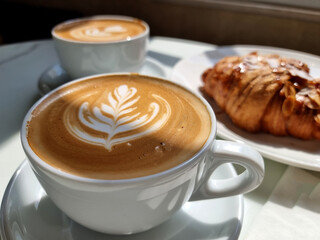 Two cups of hot latte art coffee with a croissant.