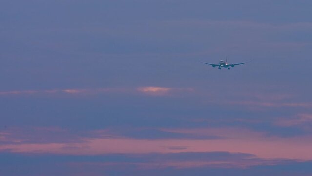 Long shot of a jet passenger plane approaching landing in a gloomy sky. Sunset or dawn, airplane in the sky. Airliner descent, arrival. Travel concept