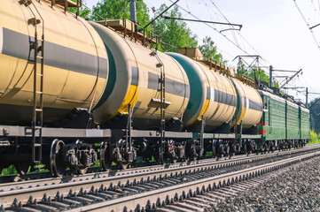 Fototapeta na wymiar The train is moving along the railway tracks. The tank car is pulled by two locomotives. Transportation of petroleum products by rail. Tanks with flammable chemical liquids. Cars with liquefied gas.