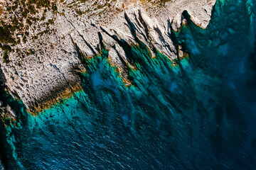 Sharp edges of rocks on the coast of the turquoise sea, flat lay view from the drone.