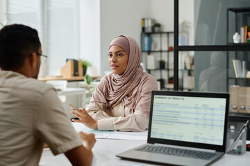 Young confident Muslim businesswoman in hijab explaining her viewpoint to male colleague and...