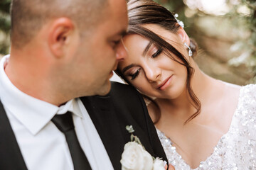 lovely and stylish newlyweds are hugging and smiling against the background of autumn nature in a beautiful garden. An incredibly beautiful young bride leaned against the shoulder of her beloved groom