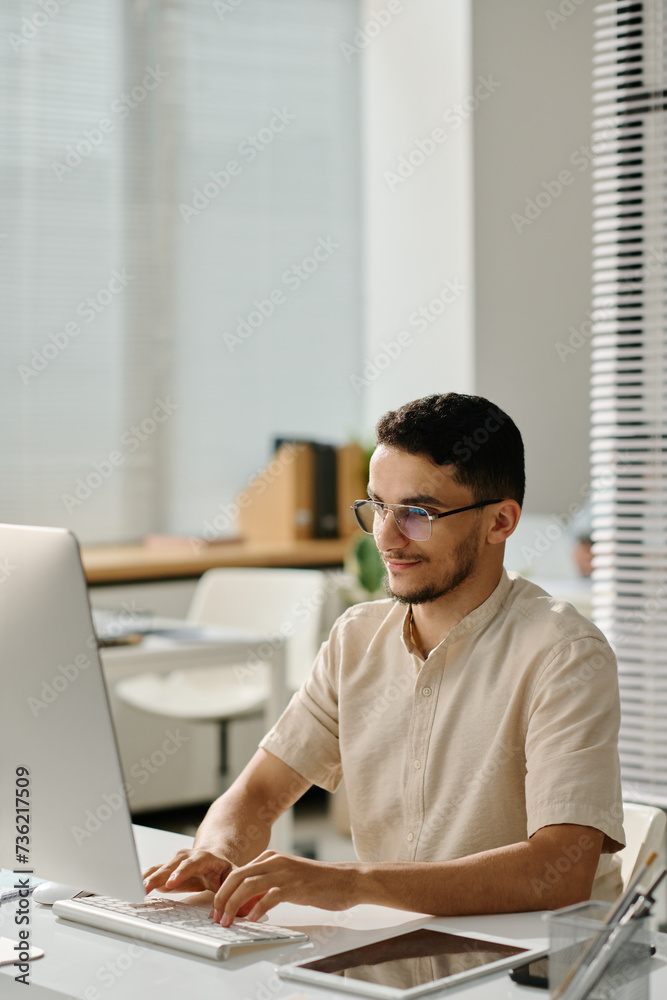 Poster young muslim male white collar worker typing on computer keyboard and looking at screen while enteri