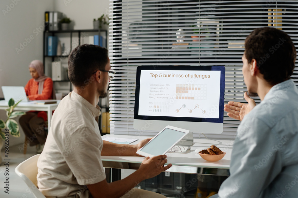 Leinwandbilder Young Muslim businessman explaining colleague statistic data while both looking at desktop computer screen during discussion