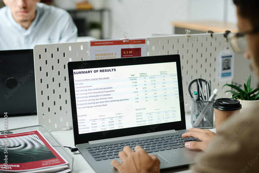 Poster laptop screen with summary of results and hands of young male economist typing on keyboard while sit