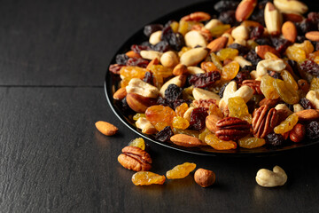 Mix of dried nuts and raisins on a black background.