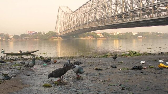 9th February, 2024, Kolkata, West Bengal, India: Beautiful landscape of a fishing boat on River Ganges crossing Howrah Bridge at the time of sunrise.