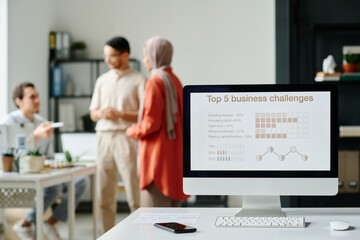 Screen of desktop computer with graphic data standing on desk against group of modern Muslim...
