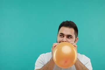 Man inflating bright balloon on turquoise background, space for text