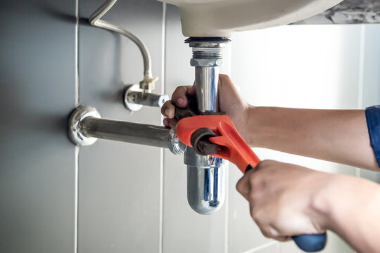 Plumber uses wrench to repair water pipe under sink There is maintenance to fix the water leak in the bathroom.with red wrench, plumbing install concept.