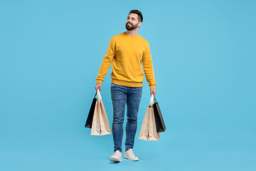 Happy man with many paper shopping bags on light blue background