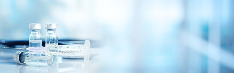 Syringe, glass vials and stethoscope on table against blurred background, space for text. Banner...