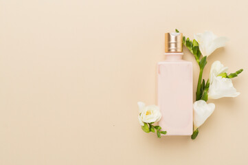 Cosmetic bottle with freesia flowers on color background, top view
