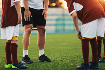 Obraz premium Group of School Kids at Fitness Class With Coach. Boys in Soccer Clothes Using Stretching Bands in Practice. Fitness Training for Youth Football Team