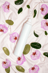 Fabric softener with floral scent among flowers on bed linen top view.