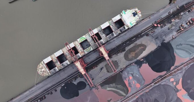 Coal and ore loading terminal with cranes and ship being loaded, birds eye aerial drone top down view. Port of Hamburg.