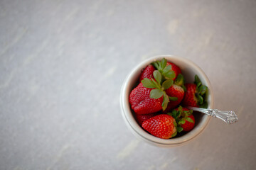 Red fresh strawberries in a white bowl with antique spoon top view on white table