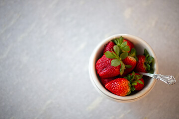 Red fresh strawberries in a white bowl with antique spoon top view on white table