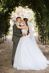 A young bride and groom tenderly embrace in the rays of the autumn sun. Tender and beautiful young girl bride. A man kisses his beloved. Against the background of a beautiful garden