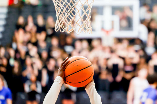 African American basketball player reaches up towards the net with orange basketball in hands 