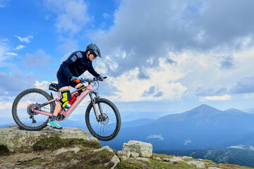 Fototapeta premium Cyclist man riding electric mountain bike outdoors. Male tourist biking along grassy trail in the mountains, wearing helmet. Concept of sport, active leisure and nature.