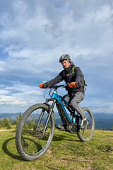 Fototapeta na wymiar Cyclist man riding electric mountain bike outdoors. Male tourist biking along grassy trail in the mountains, wearing helmet and backpack. Concept of sport, active leisure and nature.
