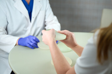 Close-up of female plastic surgeon demonstrates breast implants to a patient for her new breast. The patien holds breast silicone implants. Breast augmentation concept. Breast Implant Samples