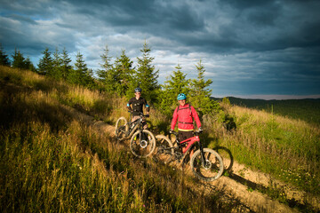 Two cyclists men riding electric bikes outdoors. Portrait of male tourists resting on the hill,...