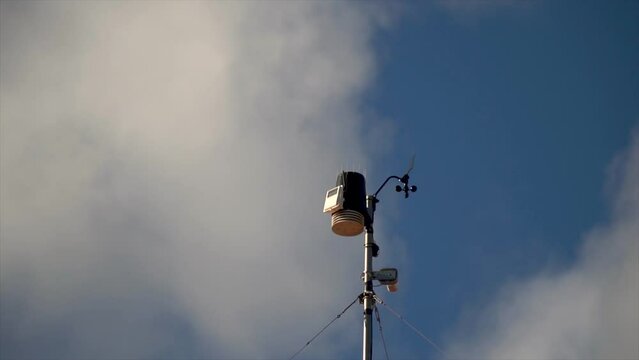 Small weather station on the roof of a house, against blue cloudy sky.